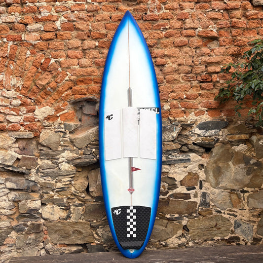 Blue Ghost Pyzel Surfboard in front of rustic stone wall.