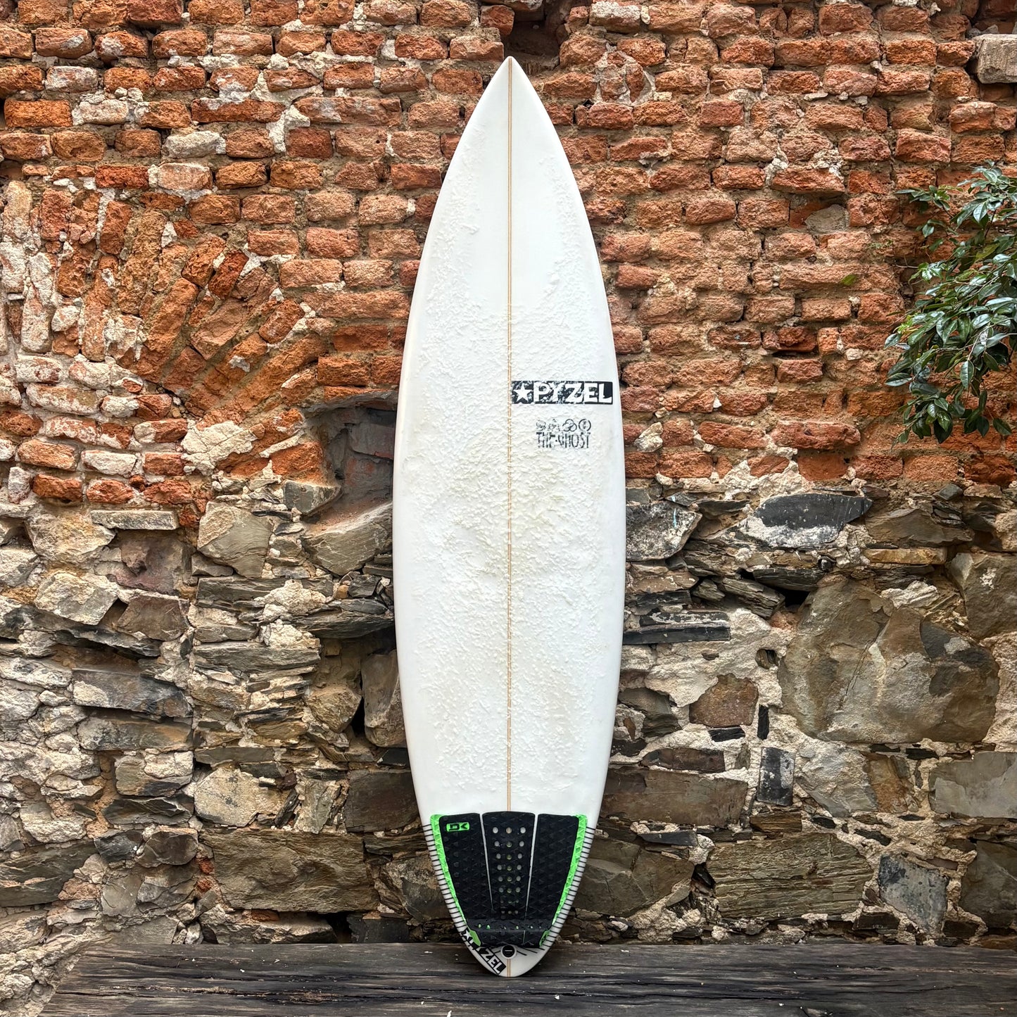 White surfboard with green accents against a rustic stone wall.