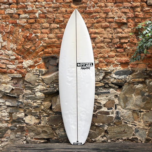A white surfboard with black Zetl branding, leaning vertically against a rustic brick and stone wall.