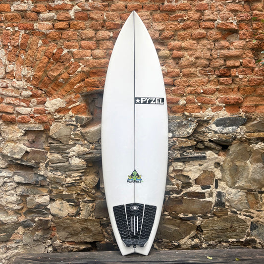 White surfboard with a logo against a rustic stone wall