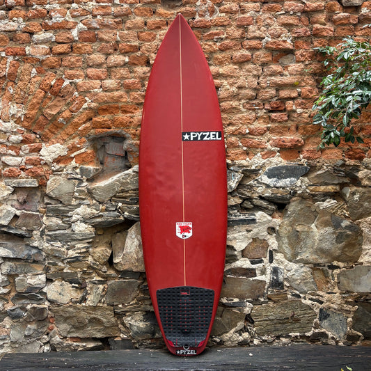 Red surfboard with a visible brand logo leaning against a stone wall.