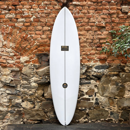 White PYZEL SCORE LORD surfboard with branding against a rustic stone wall