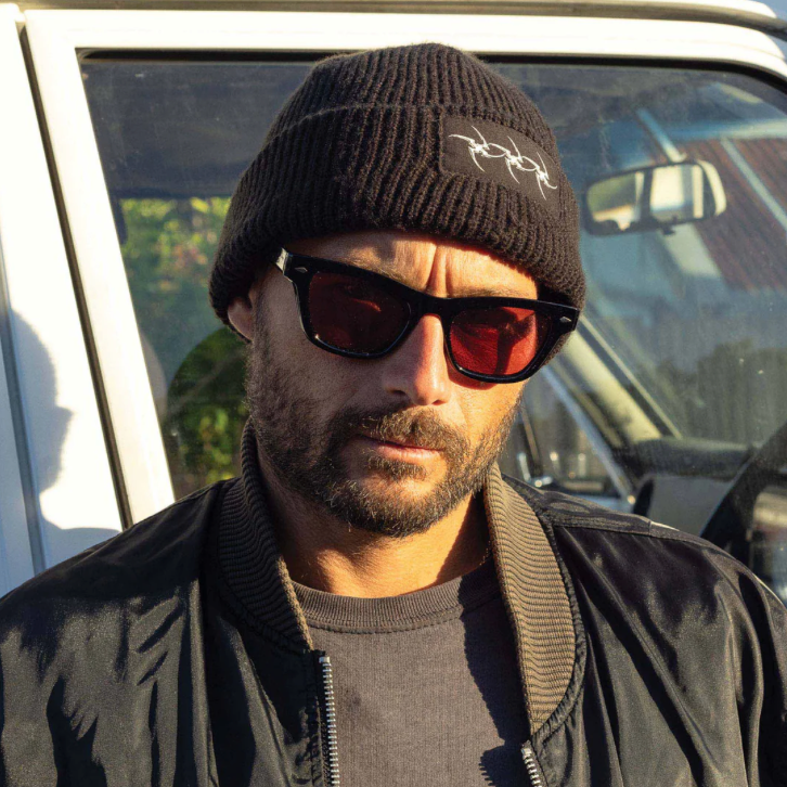 Man wearing sunglasses and a beanie in front of a vehicle