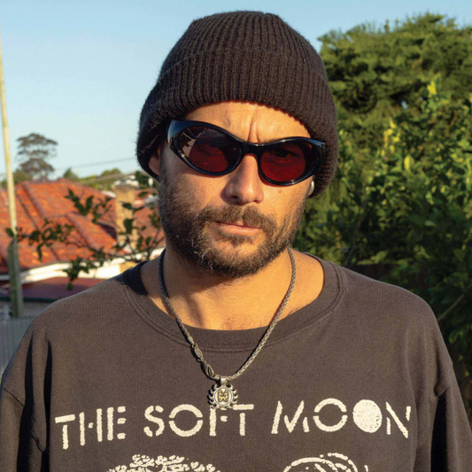 Person wearing sunglasses and a beanie with 'The Soft Moon' shirt outdoors