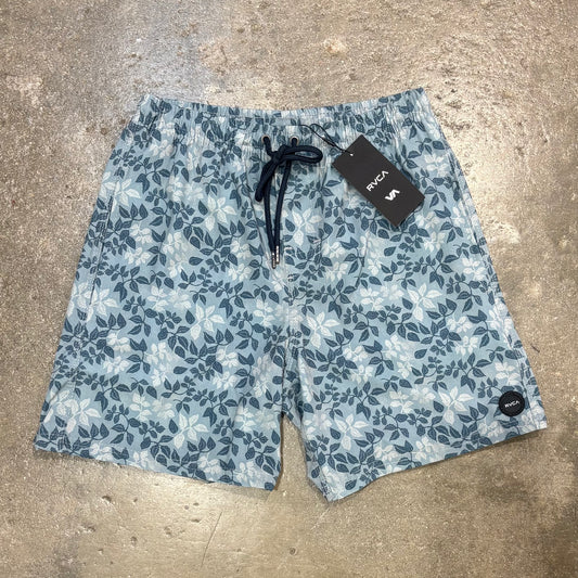 Blue floral-patterned shorts with a brand tag on a concrete surface