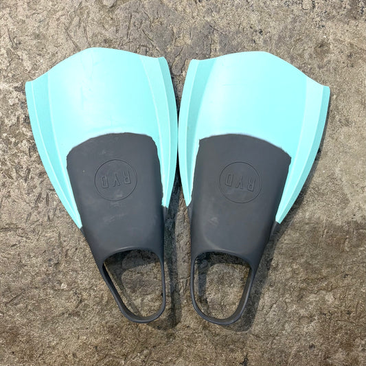 Pair of swim fins with black blades and light blue straps on a textured surface