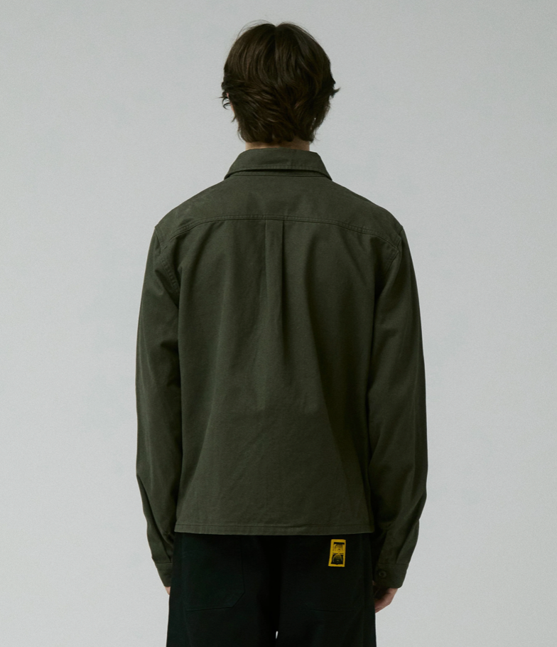 Person wearing a dark green jacket with a visible brand logo on a light gray background
