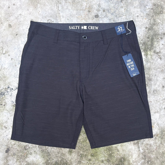 A pair of dark charcoal gray heathered shorts with 'SALTY CREW' printed on the waistband, laid flat on a textured concrete surface with a blue size and care tag attached.