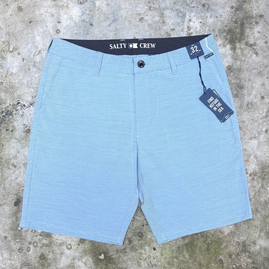 Light blue textured chino shorts with a dark navy waistband featuring the white printed brand name 'SALTY CREW', laid flat on a gray concrete surface with retail tags attached.