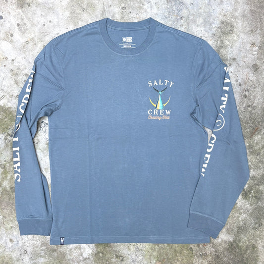 A dusty blue long-sleeve t-shirt with 'SALTY CREW' printed on the left chest and down both sleeves, laid flat on a textured gray concrete surface.