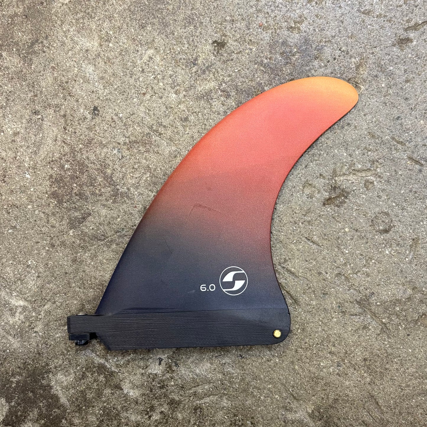 Surfboard fin with gradient color and brand logo on a concrete surface
