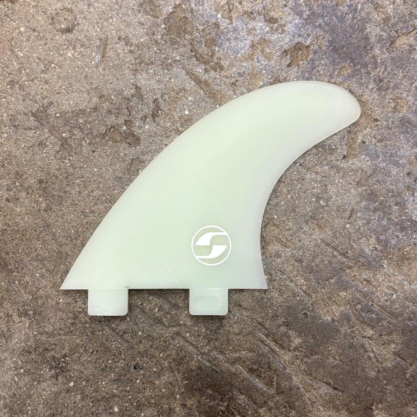 Light green surf fin with a logo on a textured brown surface