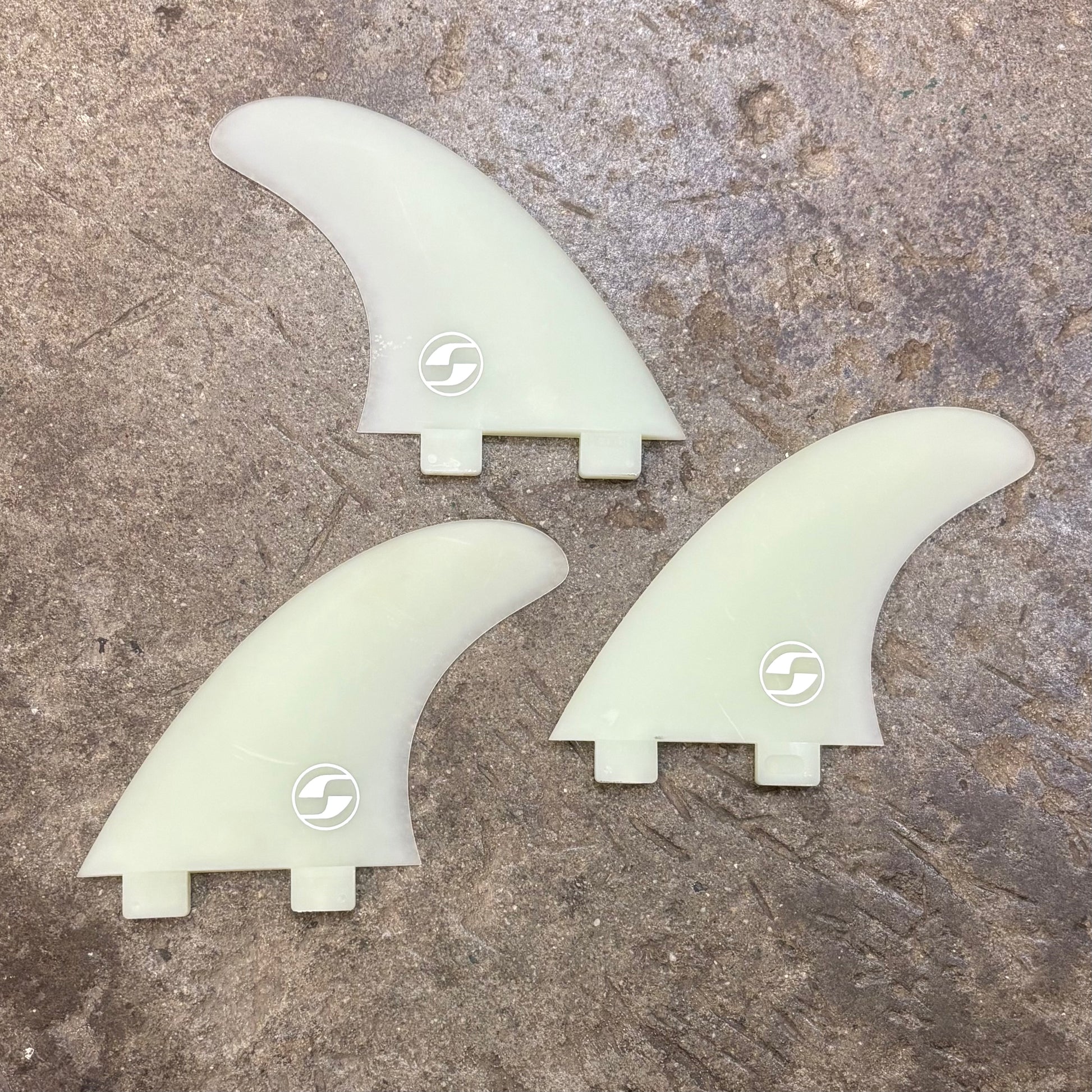 Three surfboard fins with a logo on a textured surface