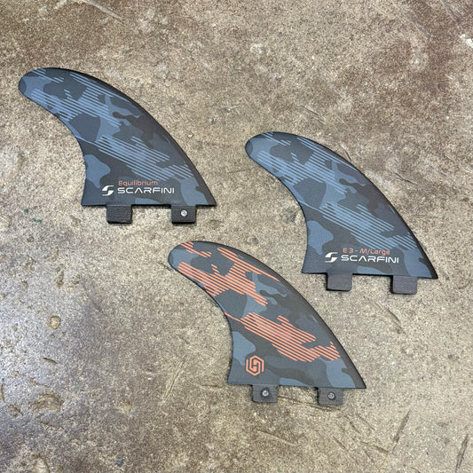 Three surfboard fins with 'Scarfini' branding on a concrete surface