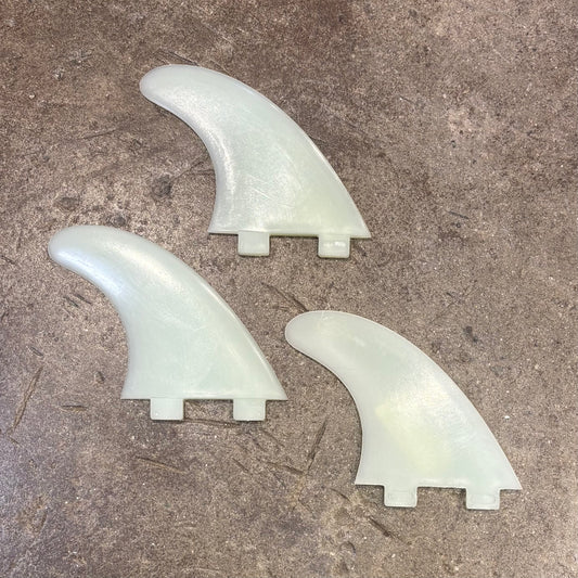 Three light-colored surfboard fins on a textured surface