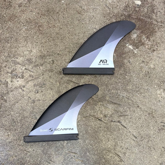 Two black and gray surfboard fins on a concrete surface