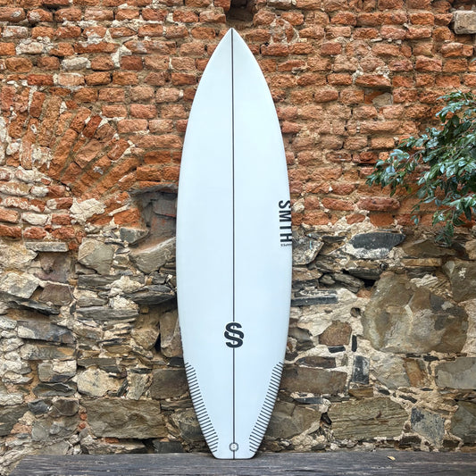 White surfboard with a logo against a rustic stone wall.