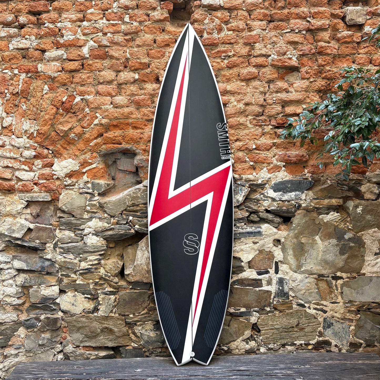 Black and red surfboard from Jordy Smith with a Union Jack design leaning against a stone wall.