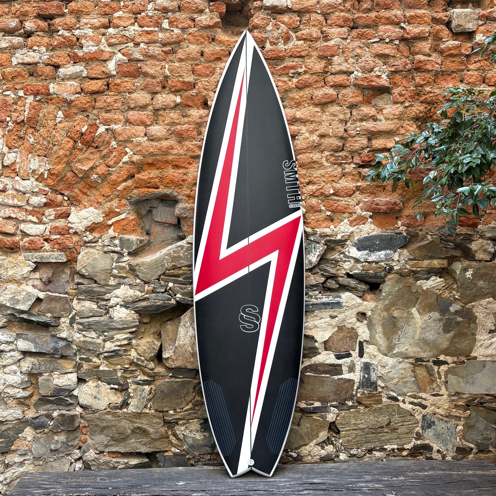 Black and red surfboard from Jordy Smith with a Union Jack design leaning against a stone wall.