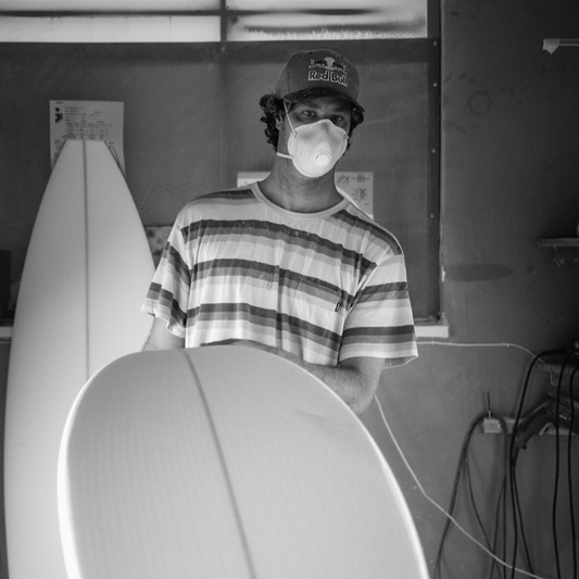 Person wearing a face mask standing behind two SMITH surfboards indoors.