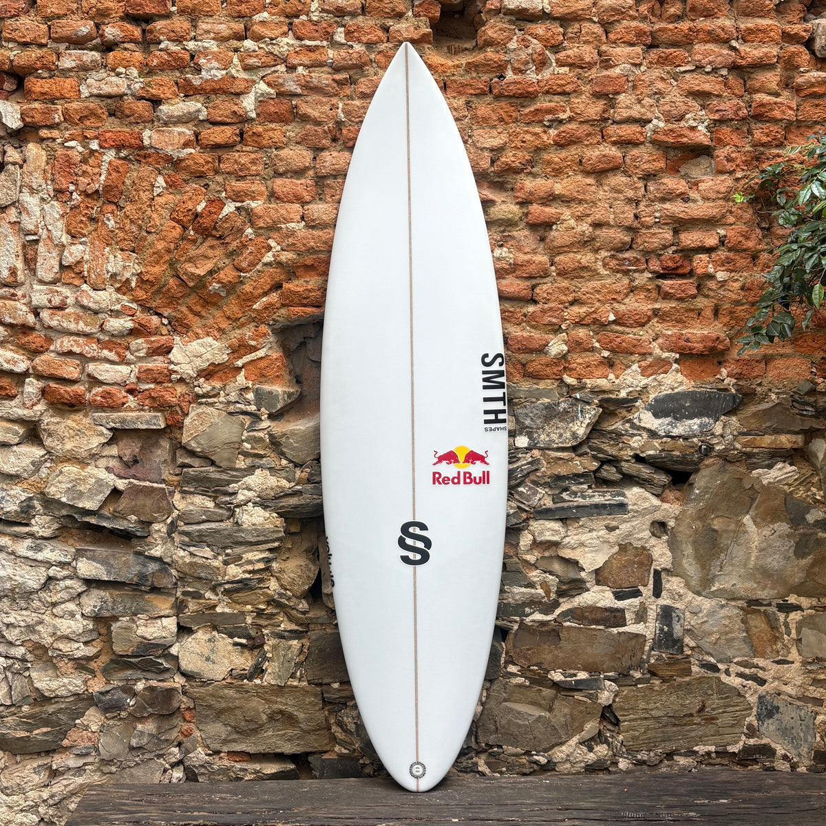 Front view of a white SMTH Shapes Volume Surfboard against a rustic wall