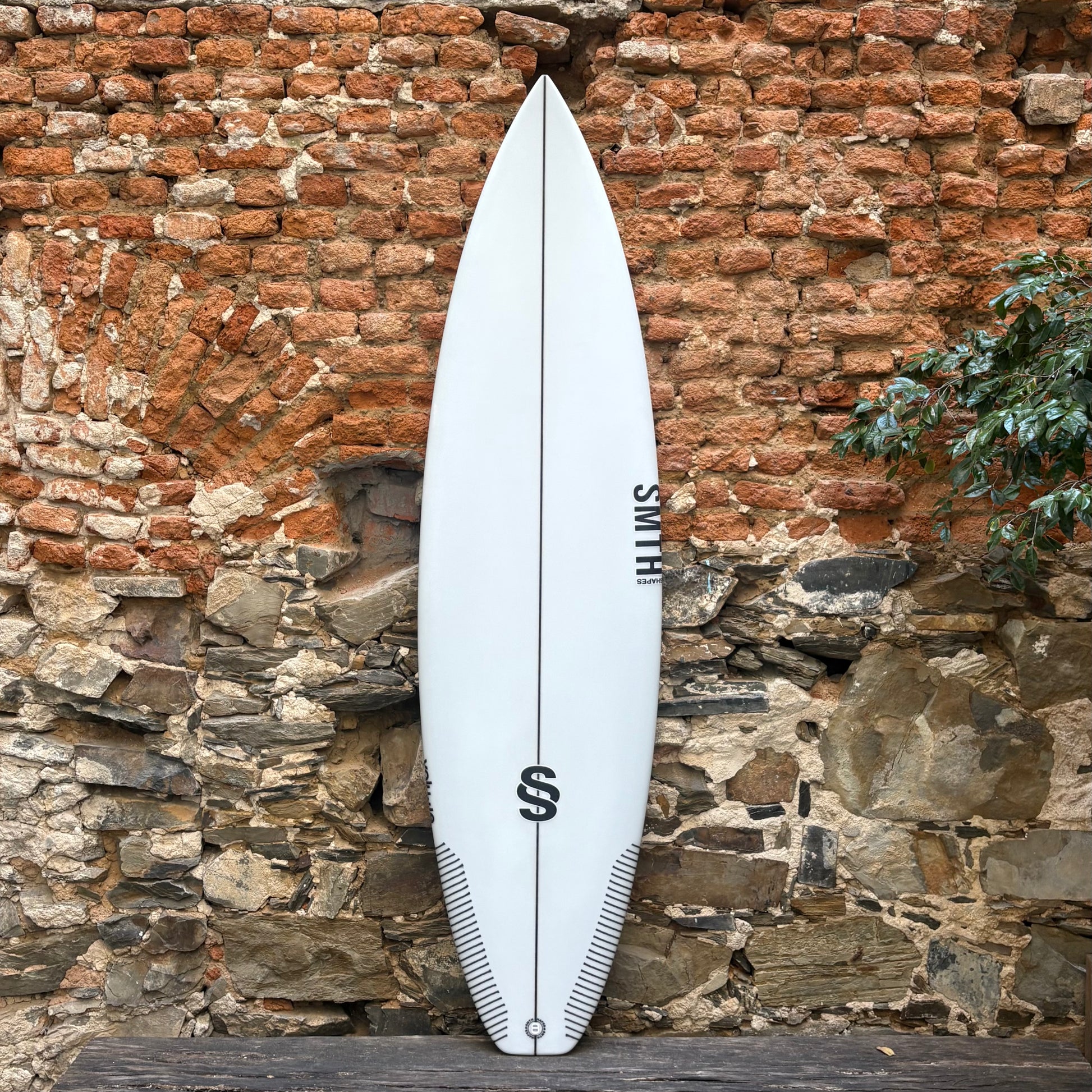 White surfboard with a logo leaning against a rustic stone wall.