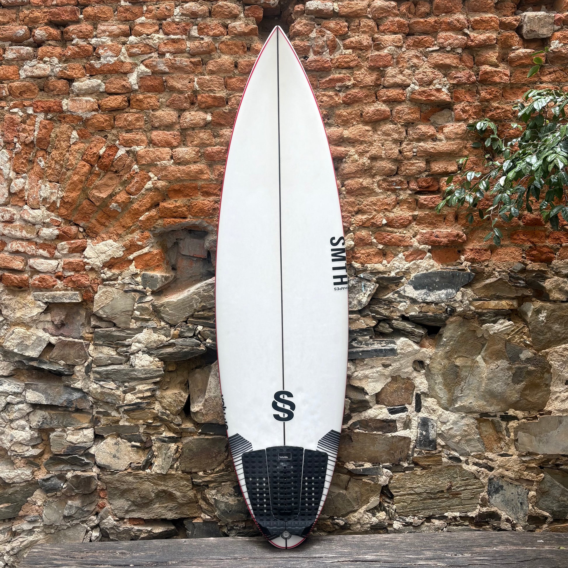 White SMTH VOLUME surfboard with black logo against a stone wall