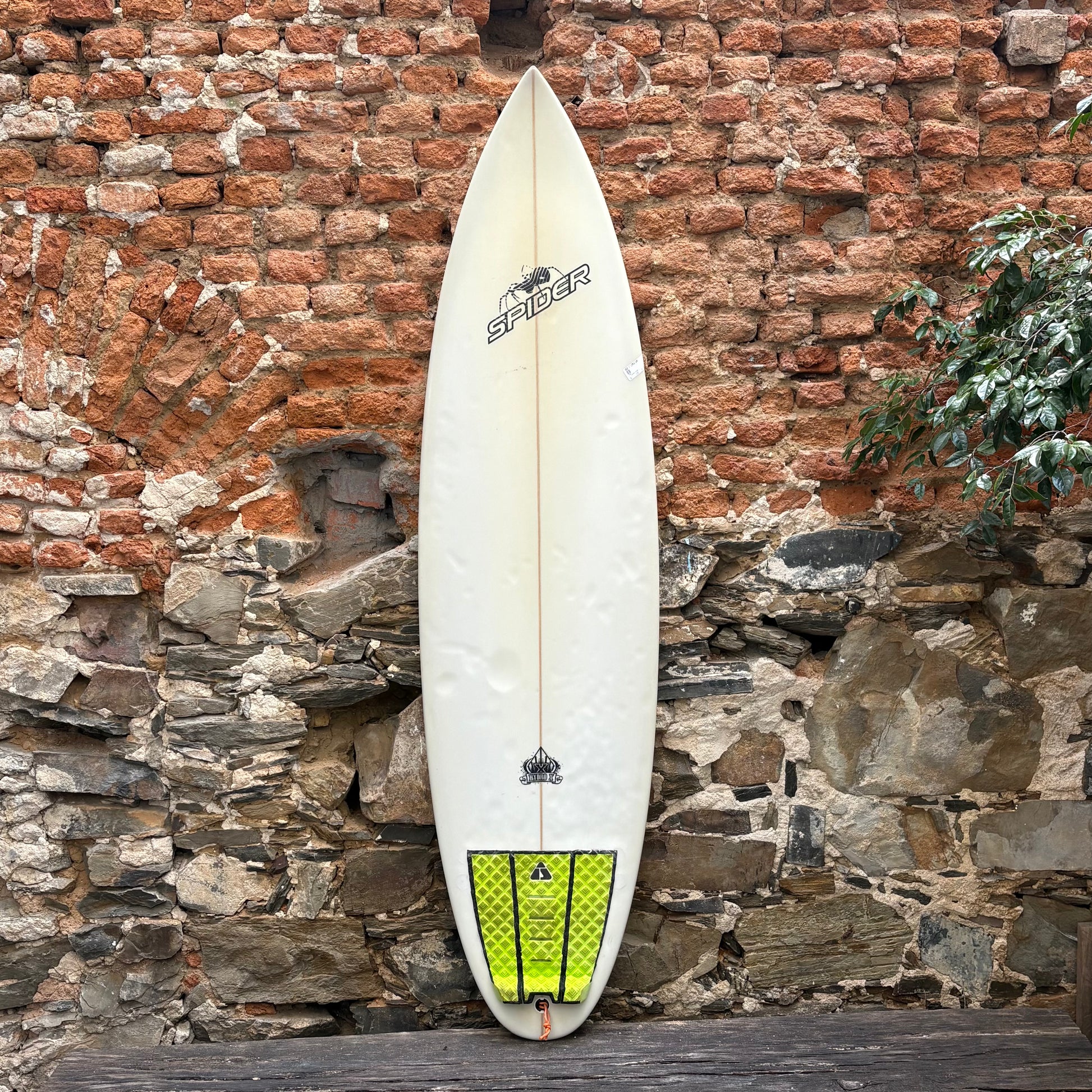 Surfboard with a green tail fin against a rustic stone wall.
