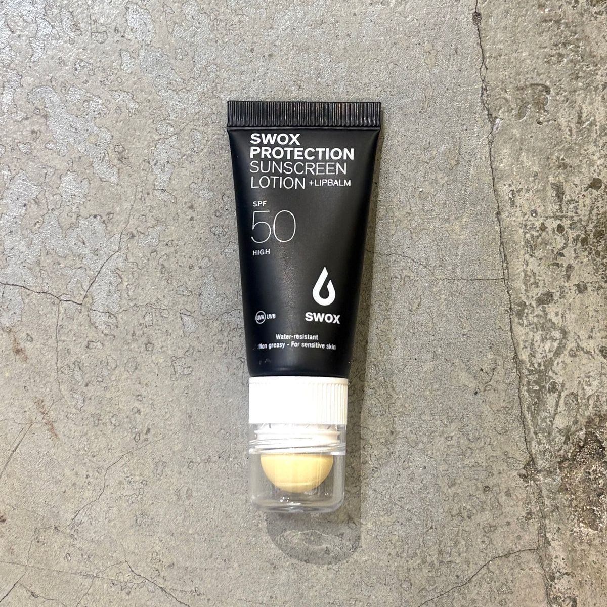 A squeeze tube of Swox Protection Sunscreen Lotion SPF 50 on a textured gray concrete surface.
