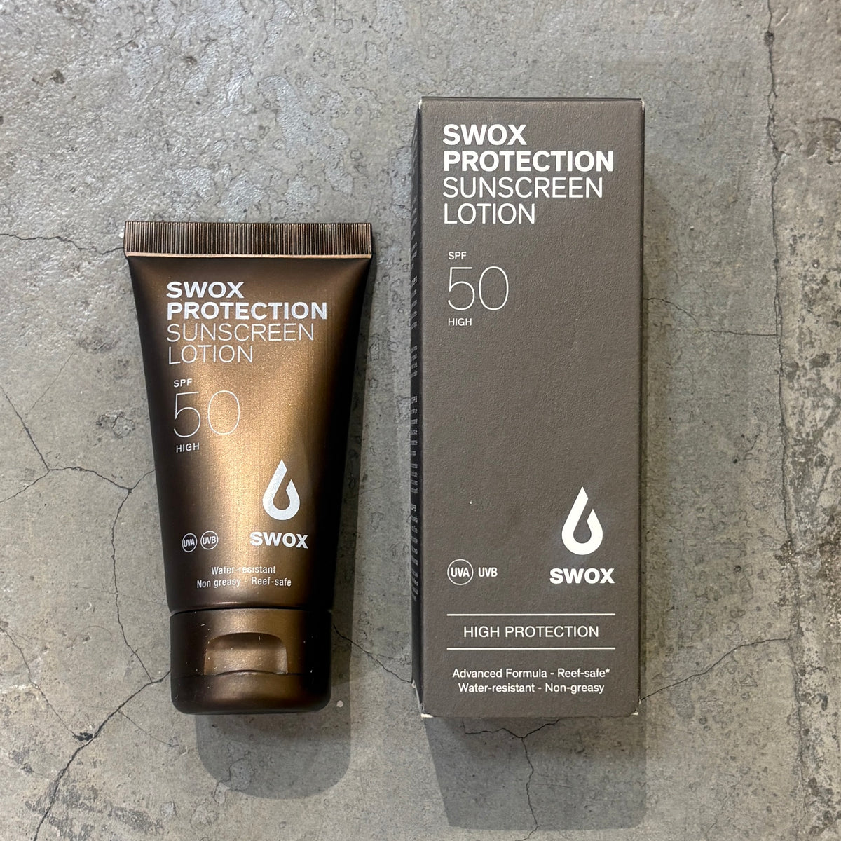 A dark brown squeeze tube and matching rectangular box of Swox Protection Sunscreen Lotion SPF 50, placed on a gray textured concrete surface.