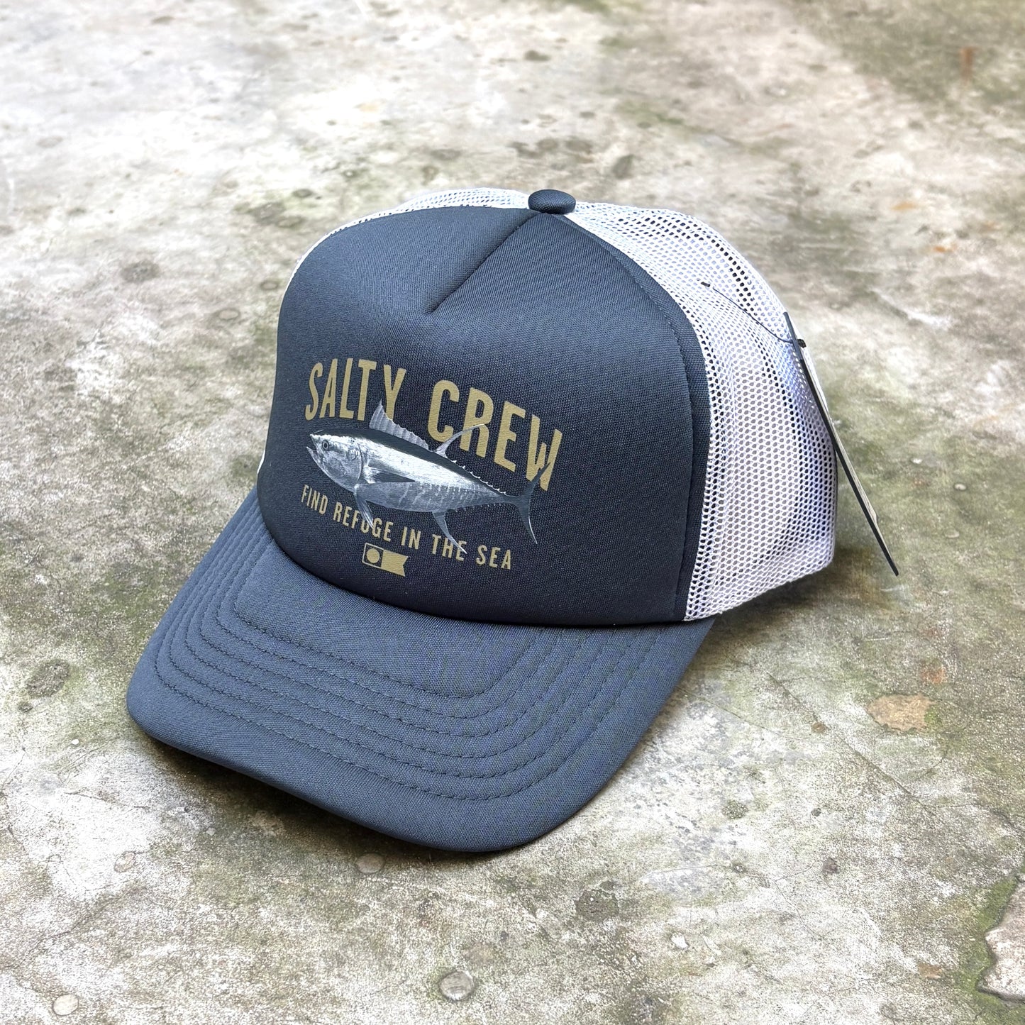 A dark slate blue and white trucker hat with a graphic of a marlin and the text 'SALTY CREW' on the front, resting on a concrete surface.