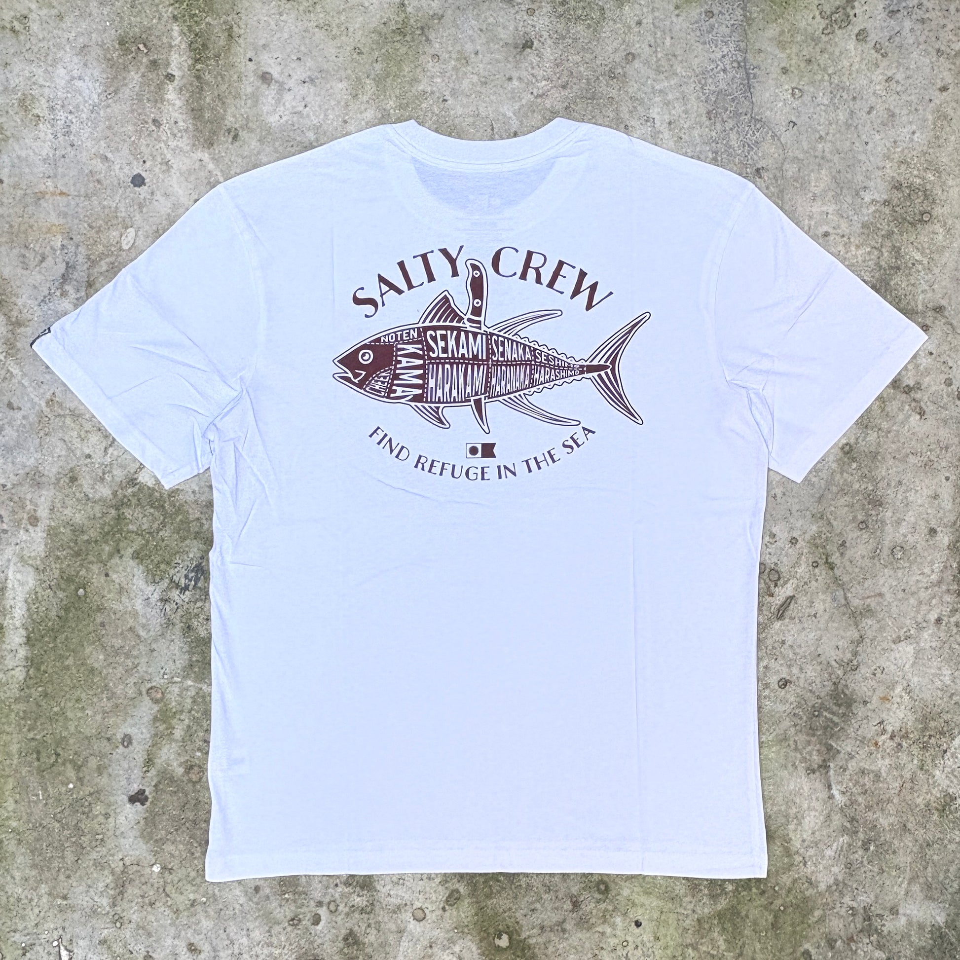 A white short-sleeve crewneck t-shirt with a dark brown graphic of a fish labeled 'SALTY CREW' and 'FIND REFUGE IN THE SEA', laid flat on a textured concrete surface.