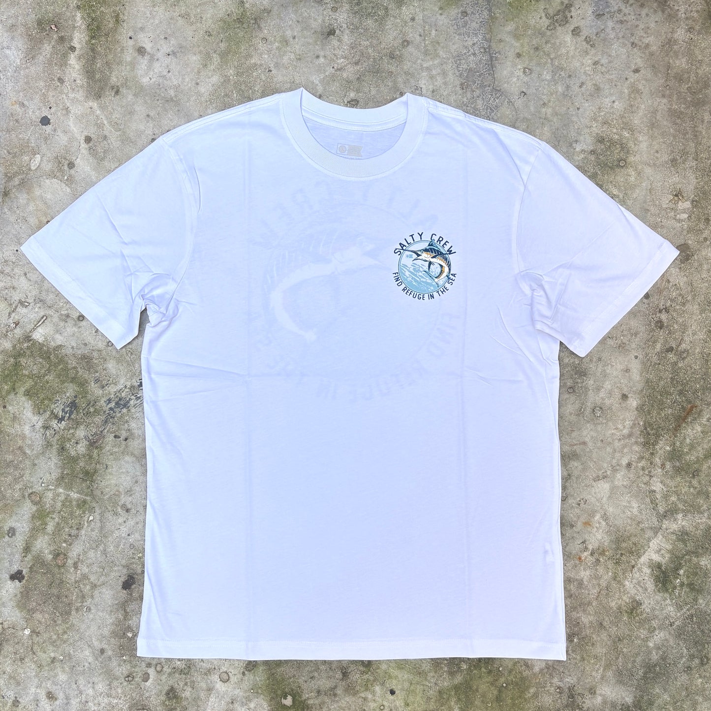 A white short-sleeve crewneck t-shirt with a light blue and white 'Saltty Rays' graphic on the left chest, laid flat on a textured concrete surface.