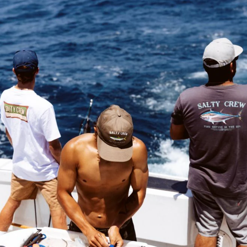 Three men on a boat wearing Salty Crew branded clothing, looking out at the ocean.