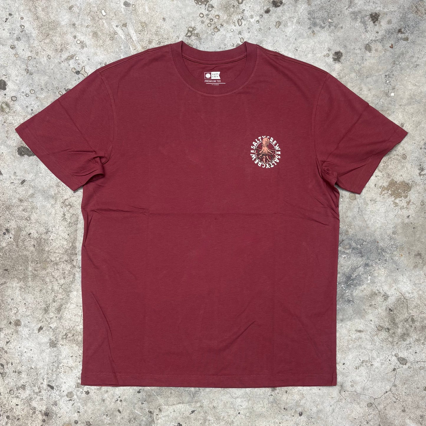 Maroon t-shirt with a small graphic on a textured surface