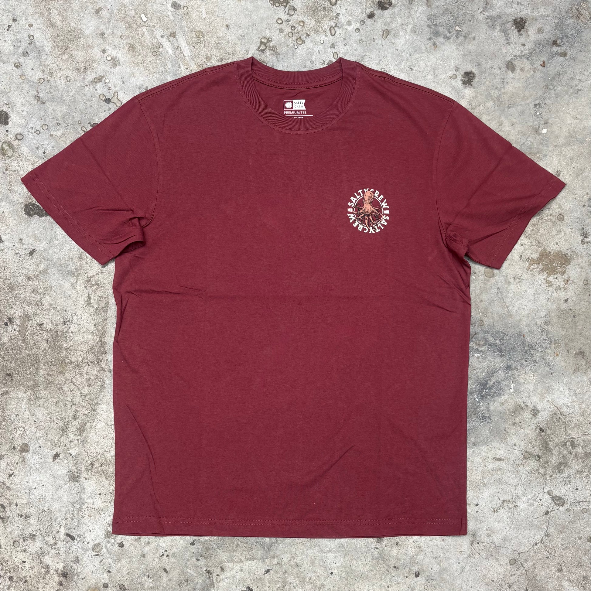 Maroon t-shirt with a small graphic on a textured surface