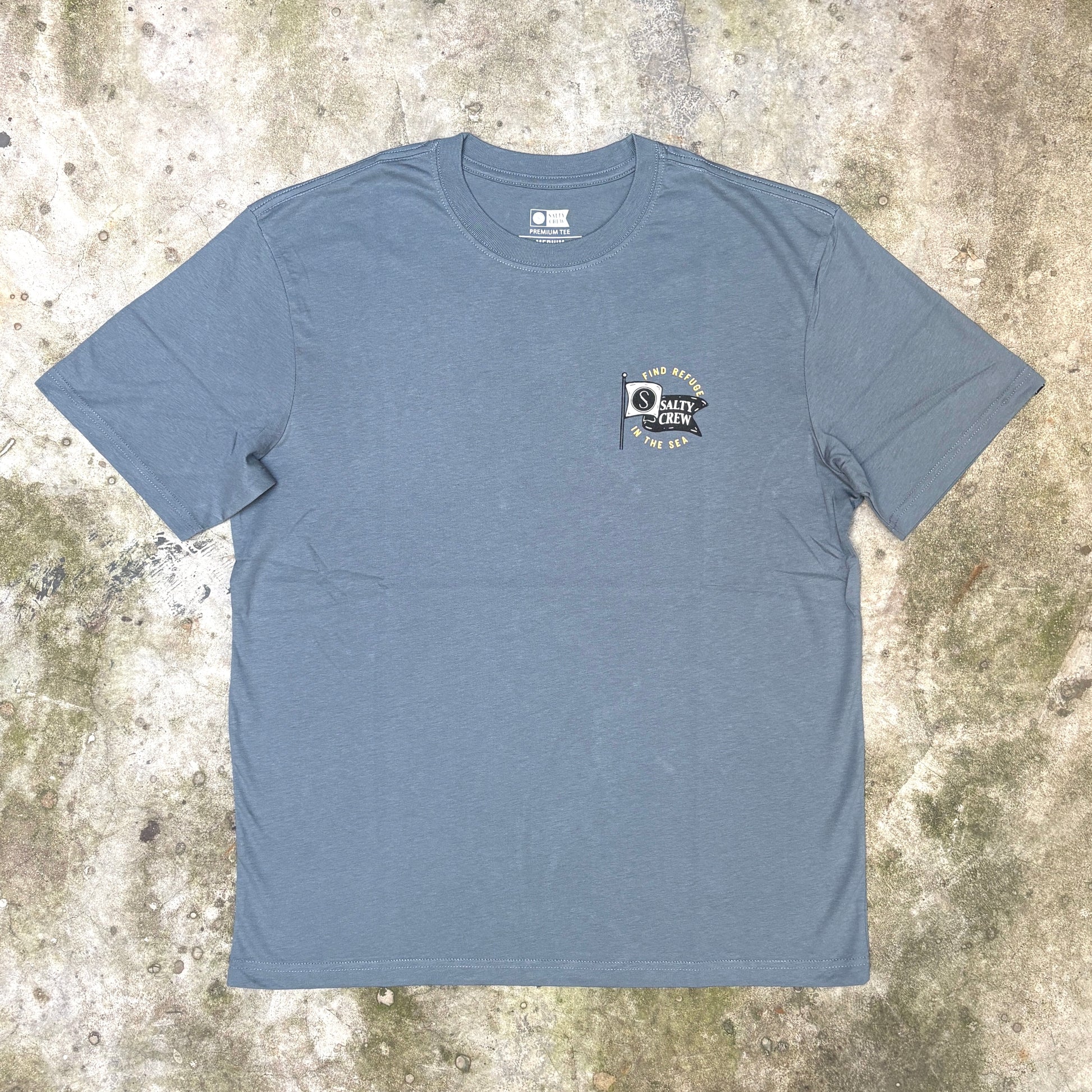 A slate blue crewneck t-shirt with a small 'Duty Star' flag graphic on the left chest, laid flat on a textured concrete surface.