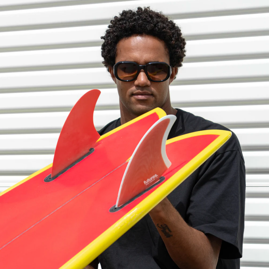 Man holding a red and yellow surfboard with fins against a white background