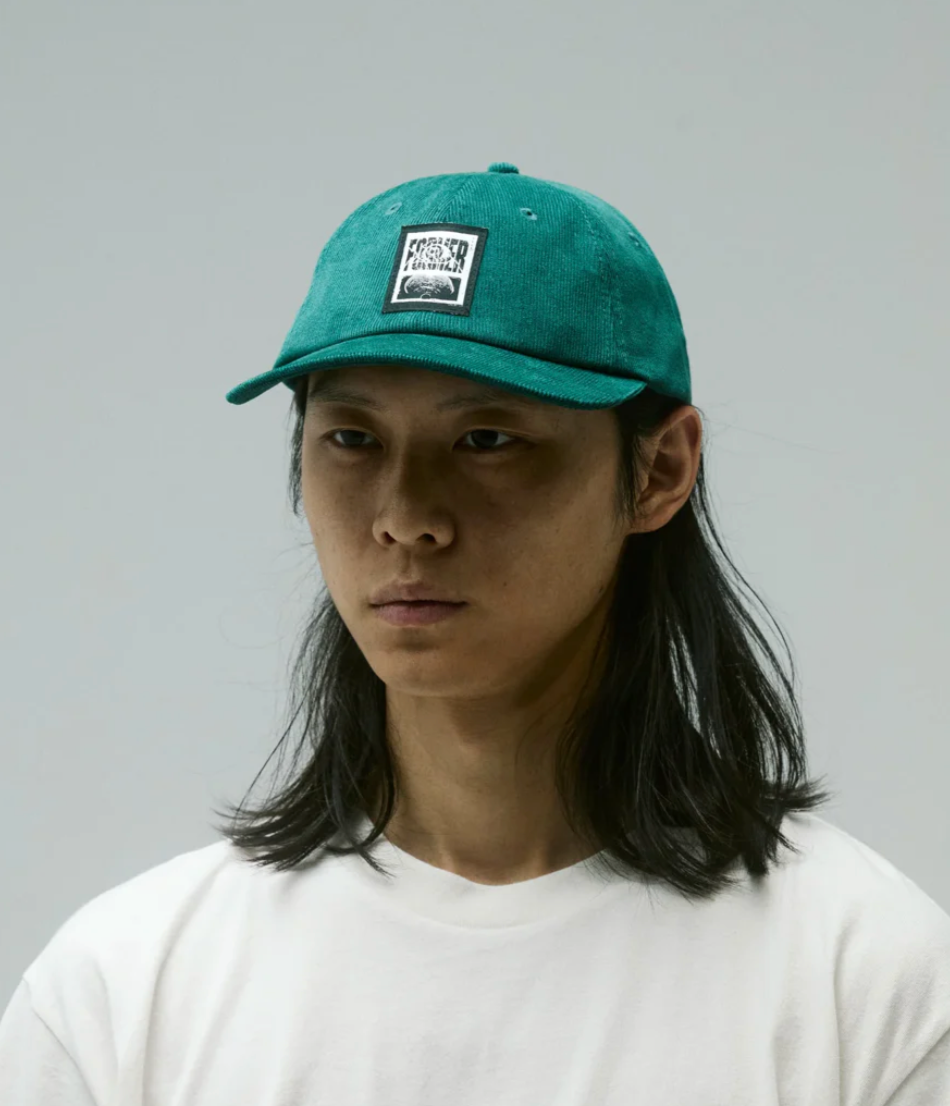 Person wearing a green cap with a Former logo on a gray background