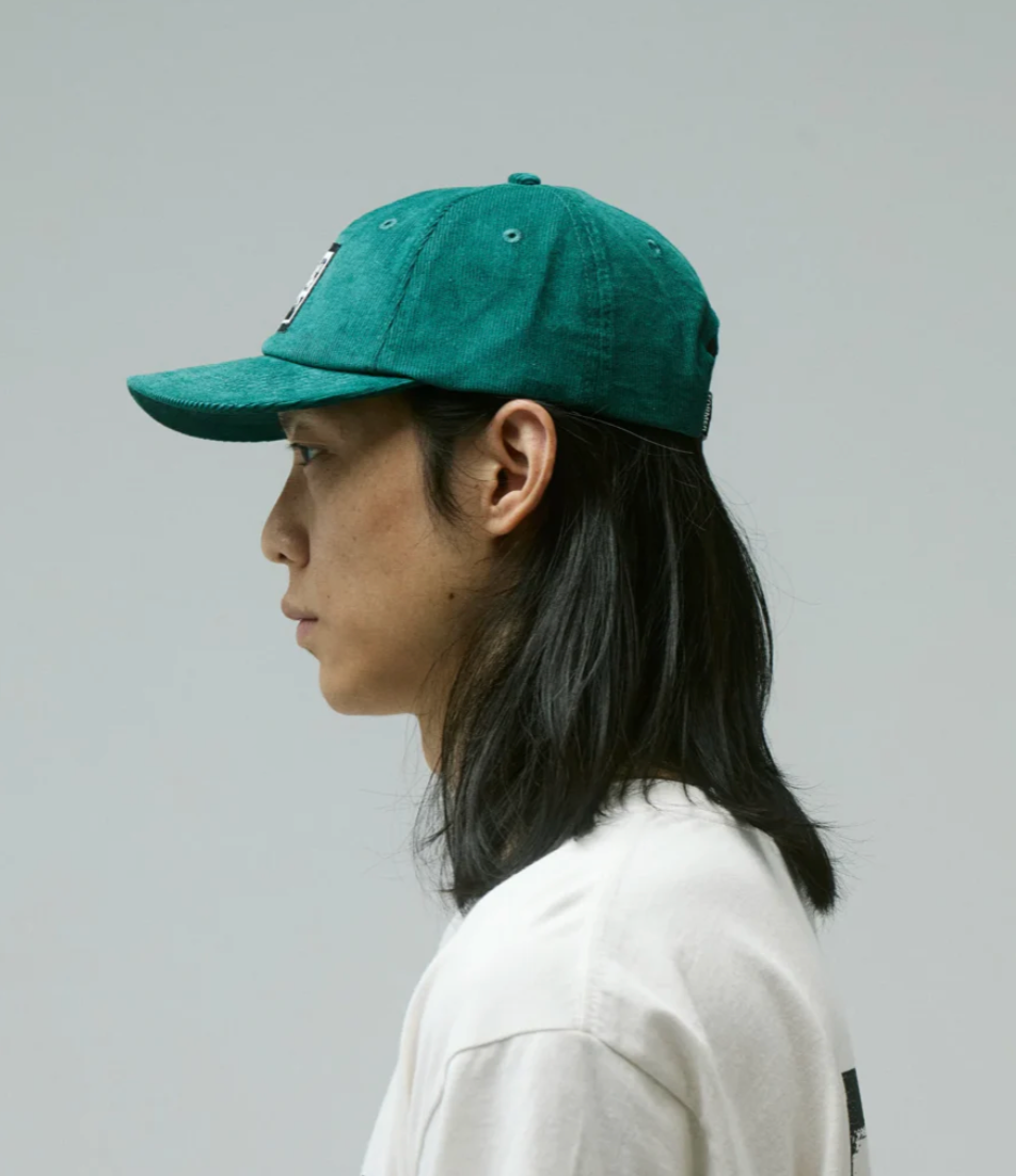 Person wearing a green Former cap and white shirt against a gray background