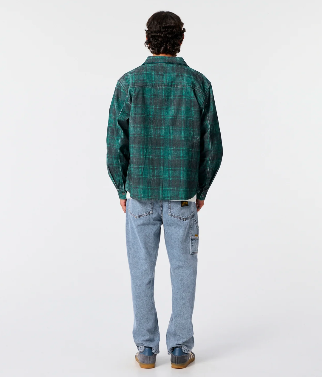 Person wearing a green plaid shirt and light blue jeans on a white background