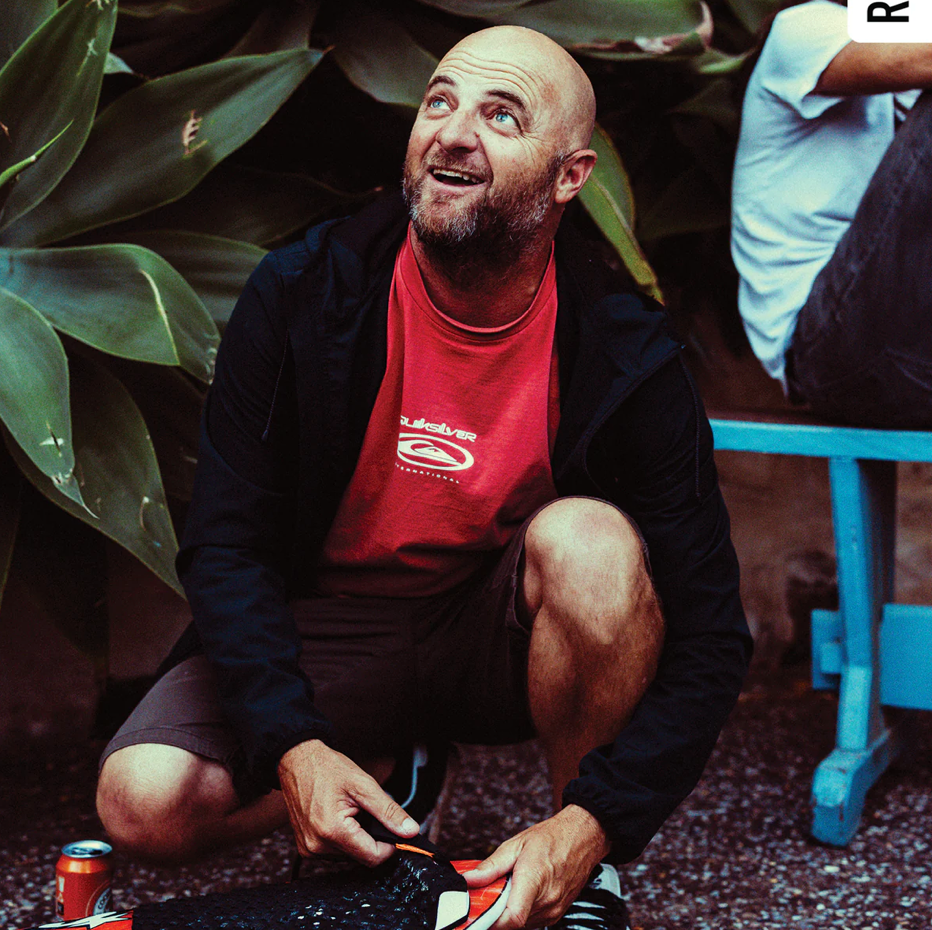 Man sitting outdoors with plants and a table in the background
