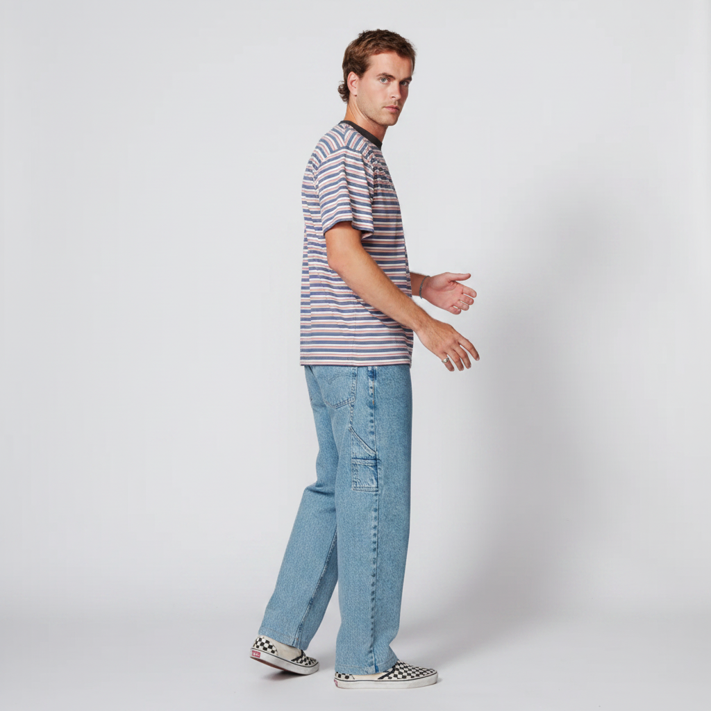 A man modeling a short-sleeve striped t-shirt with blue jeans and checkerboard slip-on shoes, standing in profile against a light gray studio background.