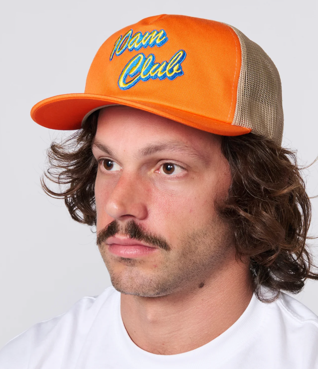 A man wearing a bright orange trucker hat with 'Dawn Club' embroidered on the front, paired with a white t-shirt against a light gray background.