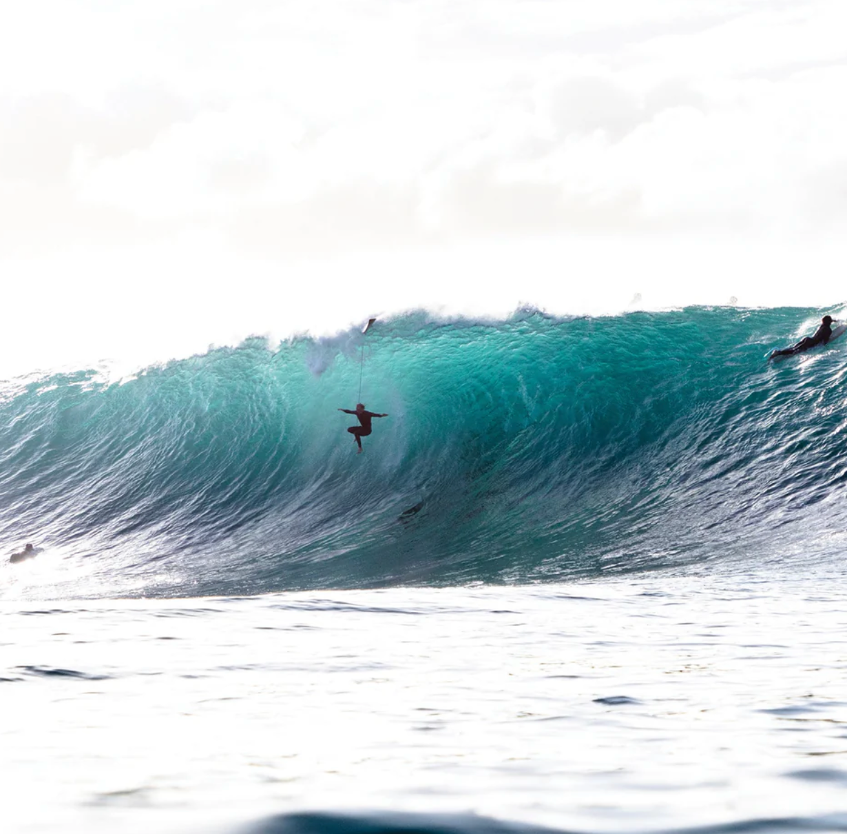 Surfer riding a large wave in the ocean with a clear sky.