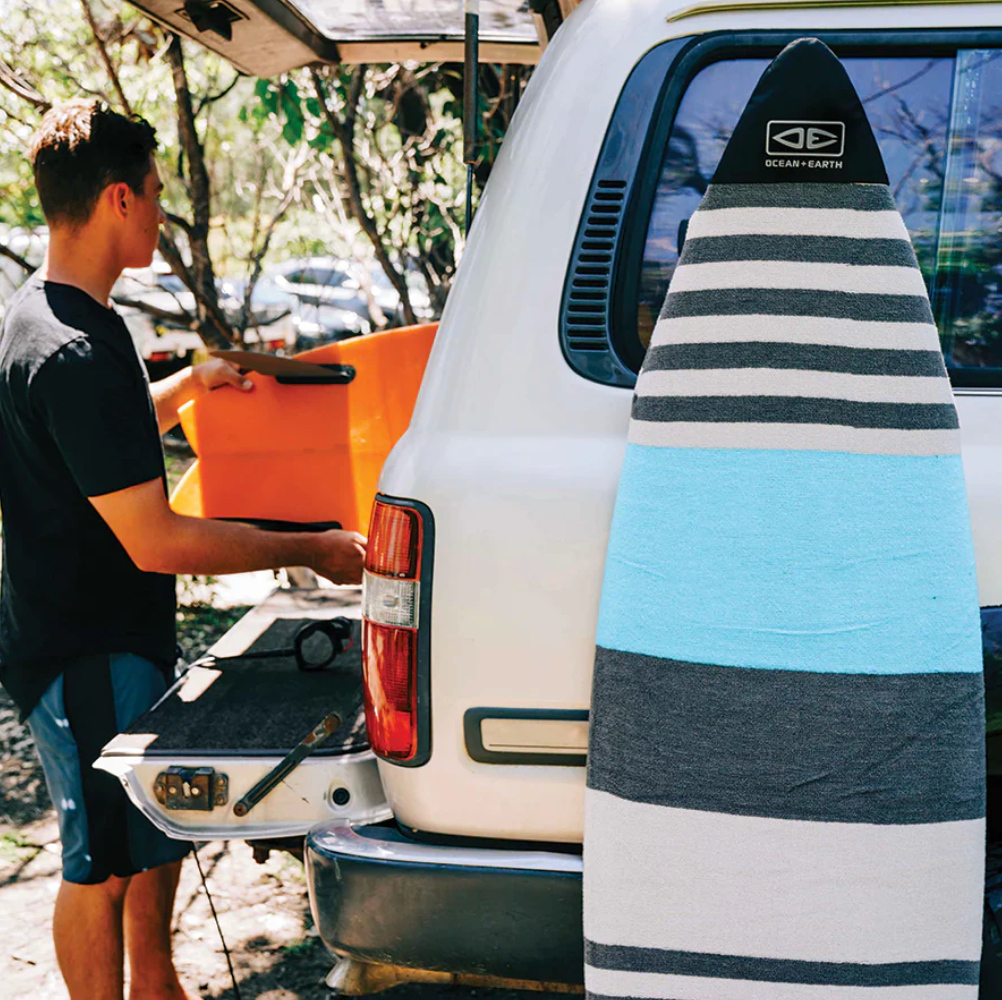Person loading an orange kayak into a white van with a striped surfboard leaning against the vehicle.
