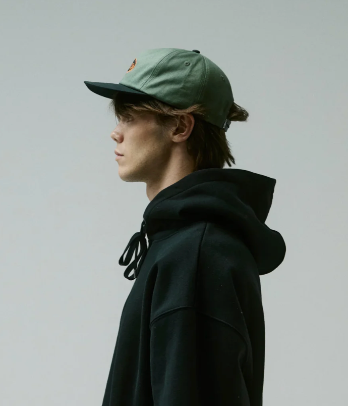 Person wearing a green cap and black hoodie against a plain background