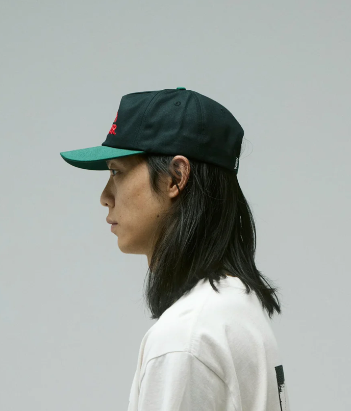 Person wearing a black cap with green brim on a plain background
