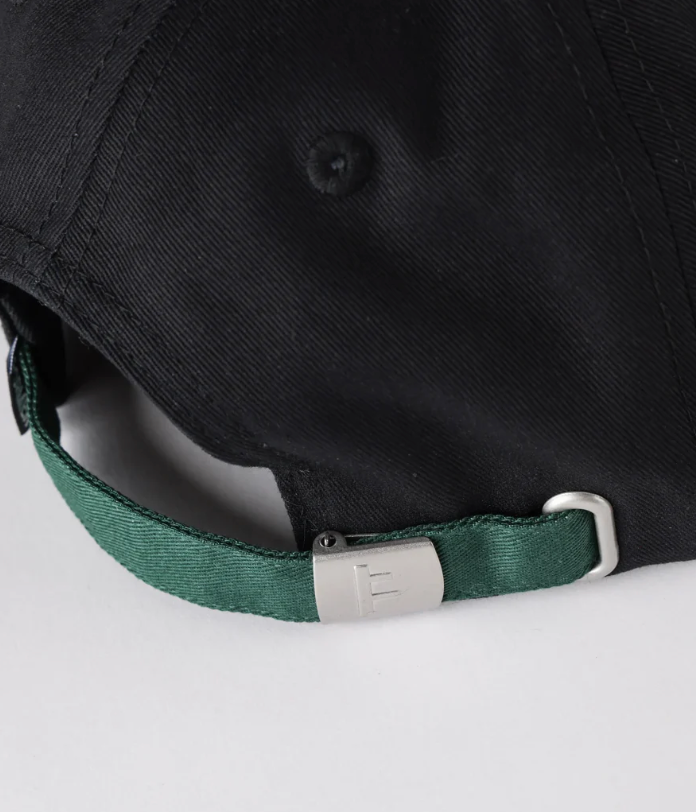 Black cap with a green strap and metal buckle on a light gray background