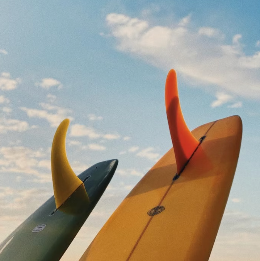 Two surfboards with fins against a cloudy sky